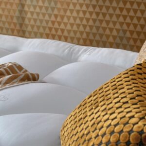 Gros plan sur le matelas EPEDA GALACTIQUE 2 160x200, dont la surface est touffetée en blanc, et qui est agrémenté d'oreillers à motifs jaunes et dorés et d'une couverture douillette.