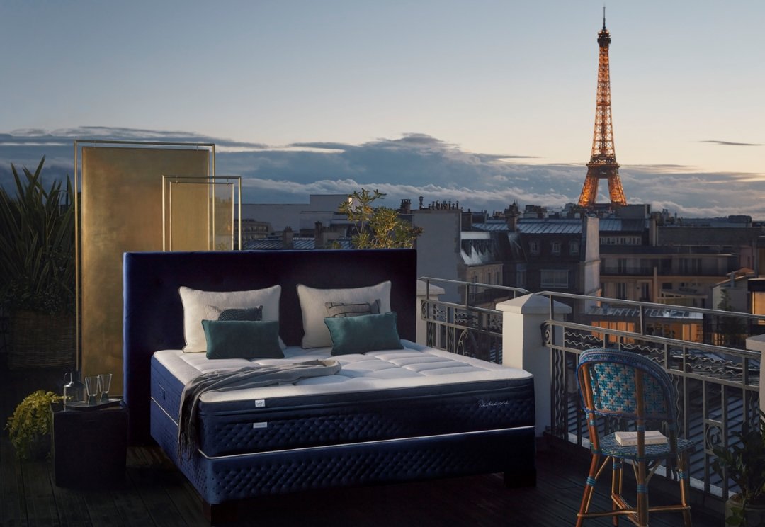 Un lit EPEDA PERSÉIDES 2 160x200 sur un balcon parisien au coucher du soleil avec la Tour Eiffel en arrière-plan.