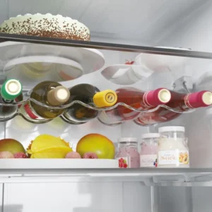 A l'intérieur du réfrigérateur HAIER HTW5618ENMG, les bouteilles de vin, les fruits, les bocaux et un gâteau sont rangés avec soin sur ses étagères spacieuses.