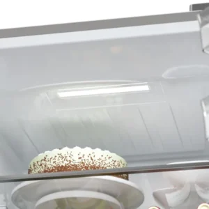 L'intérieur du réfrigérateur HAIER HTW5618ENMG présente un gâteau blanc recouvert de copeaux de chocolat placé sur une étagère en verre.