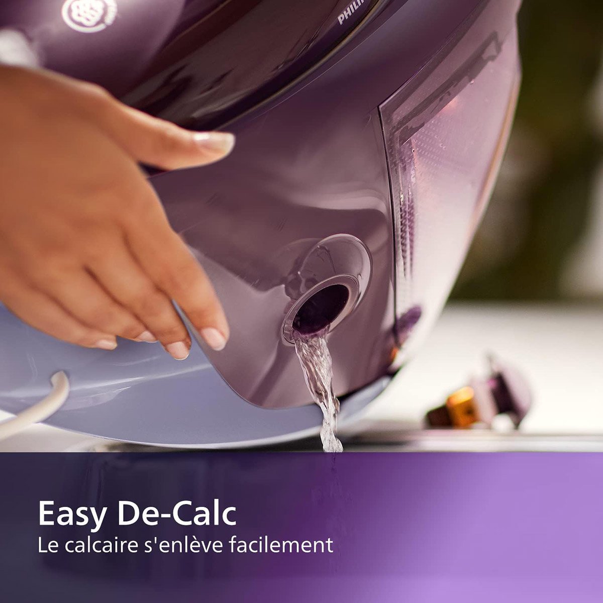 Gros plan de l'eau s'écoulant de l'orifice de décalcation d'un fer à vapeur PHILIPS PSG7150-30, avec le texte "Easy De-Calc" en dessous.