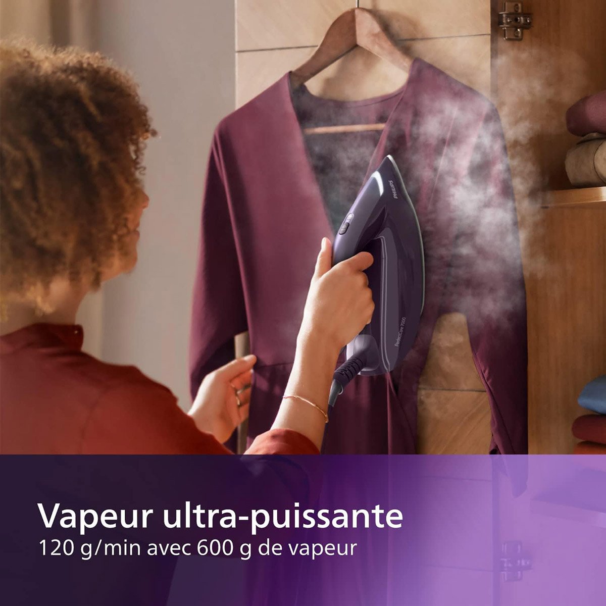 Une personne utilise le fer à vapeur PHILIPS PSG7150-30 pour défroisser une robe marron ; le texte violet affiche "Vapeur ultra-puissante".