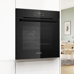 Le four encastrable BOSCH HBA571BB4 (Copie) est présenté dans une cuisine blanche élégante, avec la salle à manger visible à l'arrière-plan.