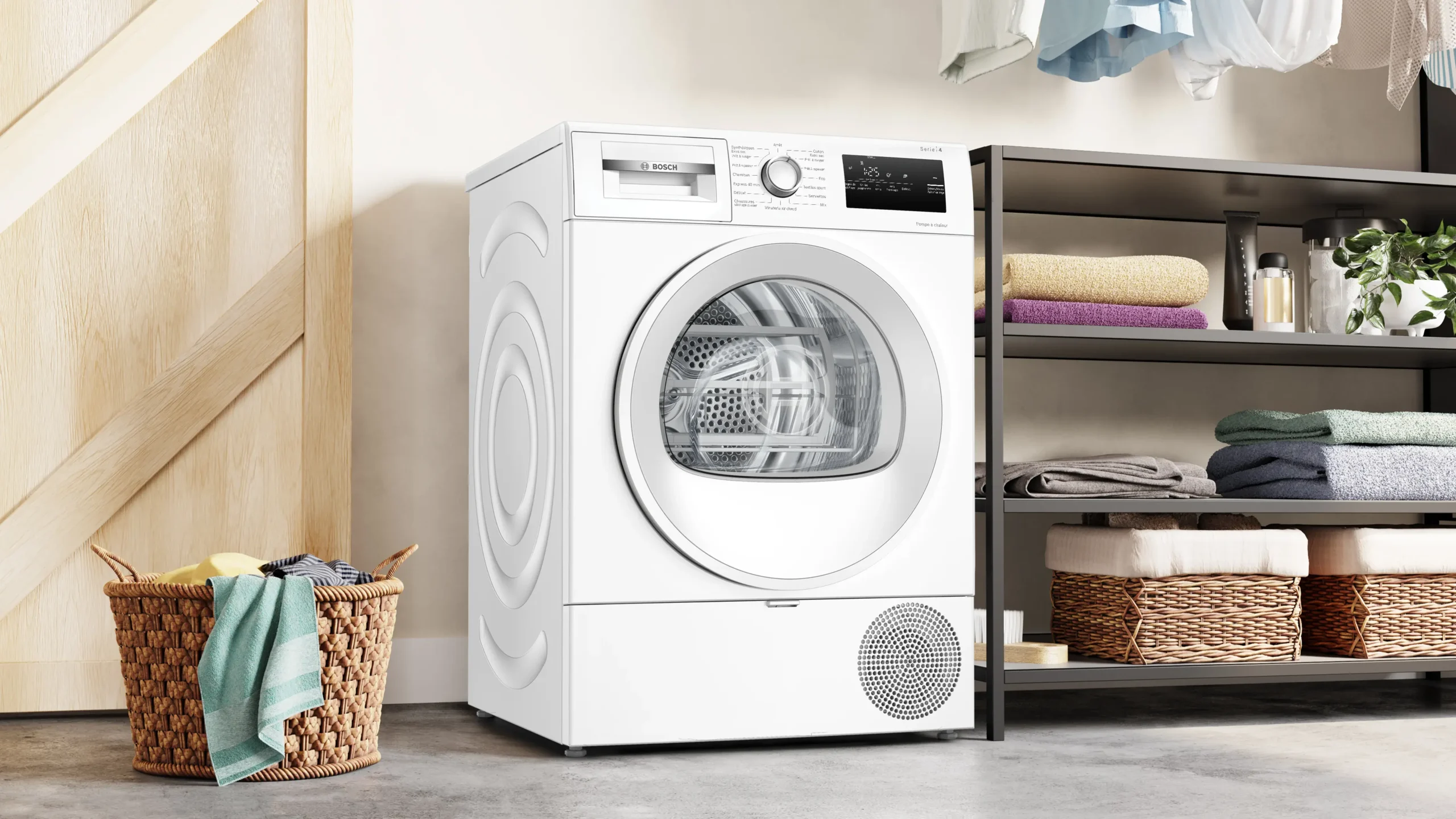 Le lave-linge séchant BOSCH WTH8520MFR blanc moderne est placé à côté d'étagères contenant des serviettes pliées et d'un panier à linge en osier posé sur le sol.
