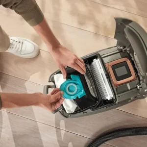 Une personne insère un sac d'aspirateur Miele GUARD L1 RED PULSE dans un aspirateur ouvert sur un sol en bois.