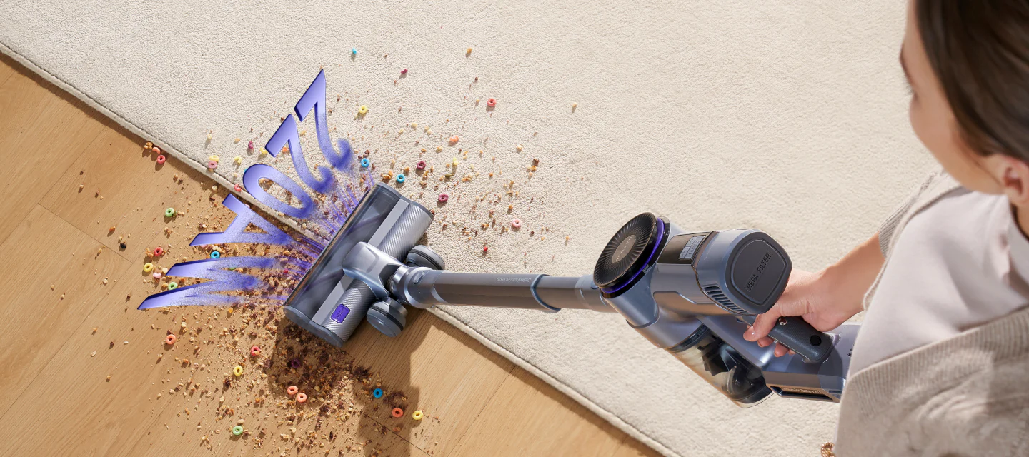 Une personne utilise un aspirateur sans fil NARWAL pour nettoyer les céréales et les miettes d'un tapis, le logo "NARWAL" étant aspiré.