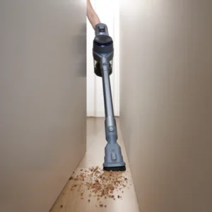 Une personne utilise l'aspirateur sans fil NARWAL pour nettoyer les miettes sur le sol dans un espace restreint entre deux meubles.