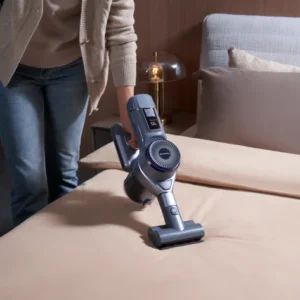 Une personne utilise un aspirateur à main NARWAL pour nettoyer un lit soigneusement fait avec des draps beiges.