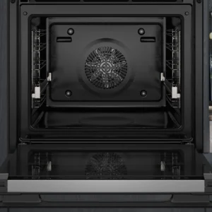Le four encastrable SIEMENS HB978GNM1 est présenté avec sa porte ouverte, révélant un intérieur impeccable et un ventilateur circulaire à l'arrière, soulignant sa conception avancée.