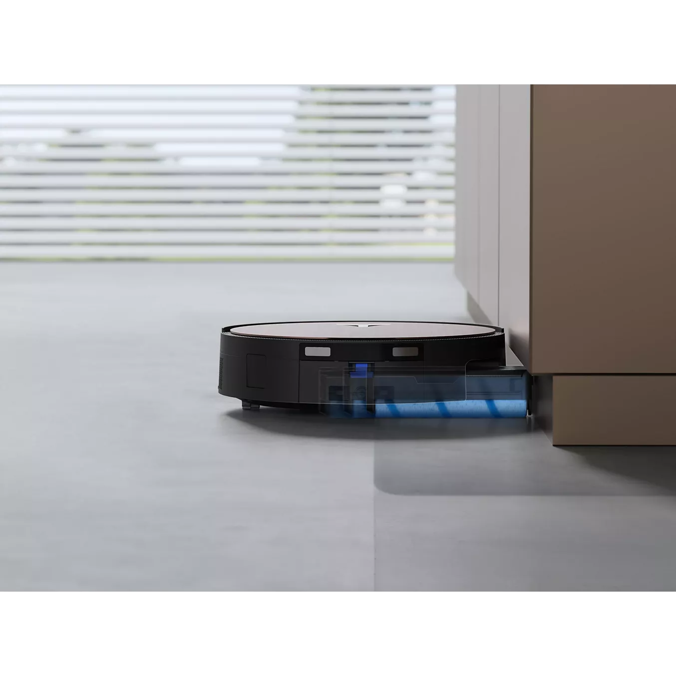 L'ECOVACS X11 omni, un aspirateur robot intelligent, se déplace sur le sol près d'une armoire dans une pièce moderne et lumineuse avec de grandes fenêtres et des stores élégants.