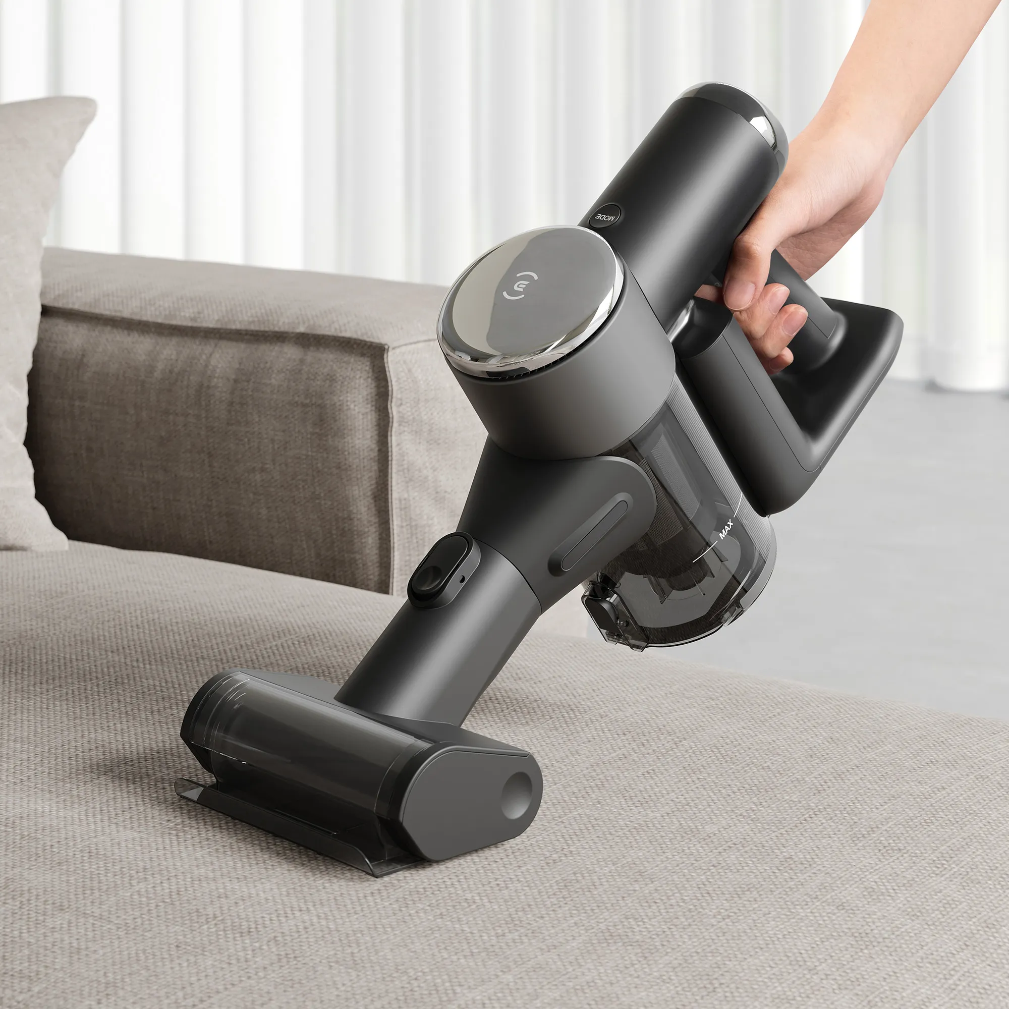 Une personne utilise l'aspirateur sans fil ECOVACS X2 COMBO pour nettoyer un canapé en tissu gris clair, s'attaquant aux dégâts que votre robot pourrait manquer - le duo parfait pour des espaces de vie impeccables.