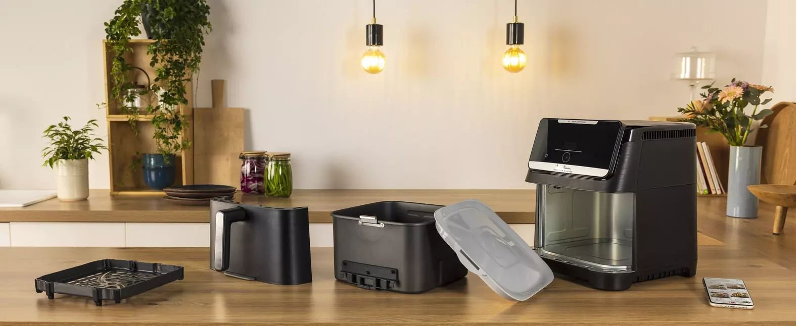 La friteuse MOULINEX EZ8428F0, de couleur noire, est présentée sur un comptoir de cuisine avec son panier, son plateau et son couvercle séparés.