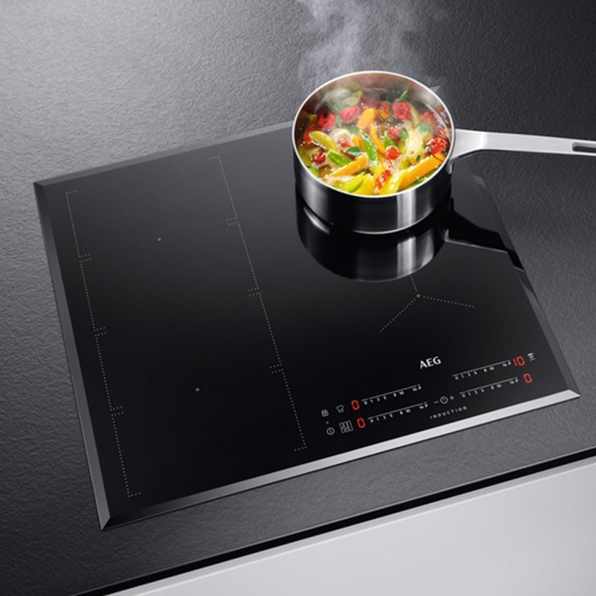 Les légumes colorés cuisent sur la plaque à induction AEG IKE64471FB noire et élégante, dotée de commandes numériques.