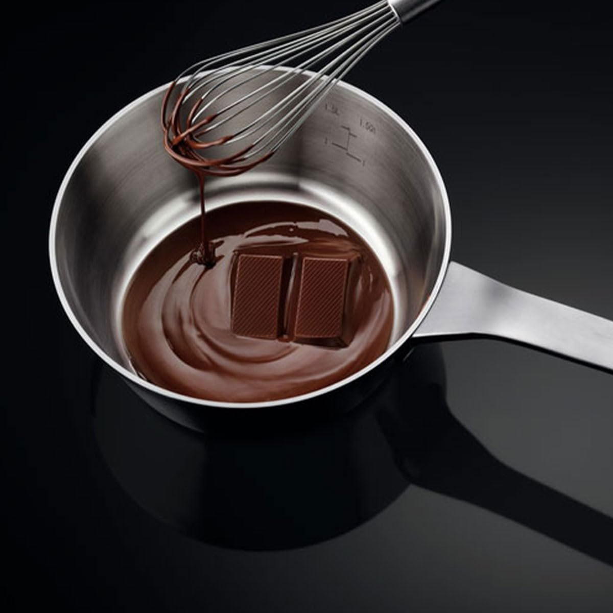 Les carrés de chocolat fondent dans une casserole sur la plaque à induction AEG IKE64471FB, tandis qu'un fouet les recouvre de chocolat fondu.