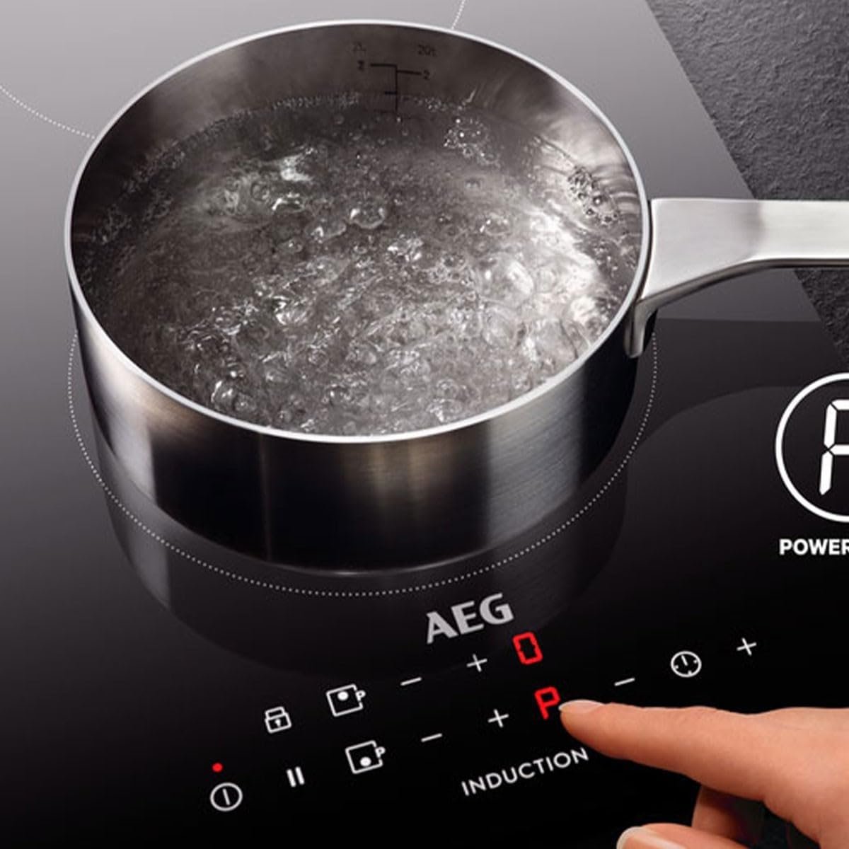 Une main appuie sur les boutons de l'AEG IKE64471FB tandis qu'une casserole d'eau bout sur sa surface à induction.
