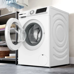 Un lave-linge moderne BOSCH WGG254FAFR (Copie) à chargement frontal avec la porte ouverte est présenté dans une buanderie avec des étagères de serviettes soigneusement pliées.