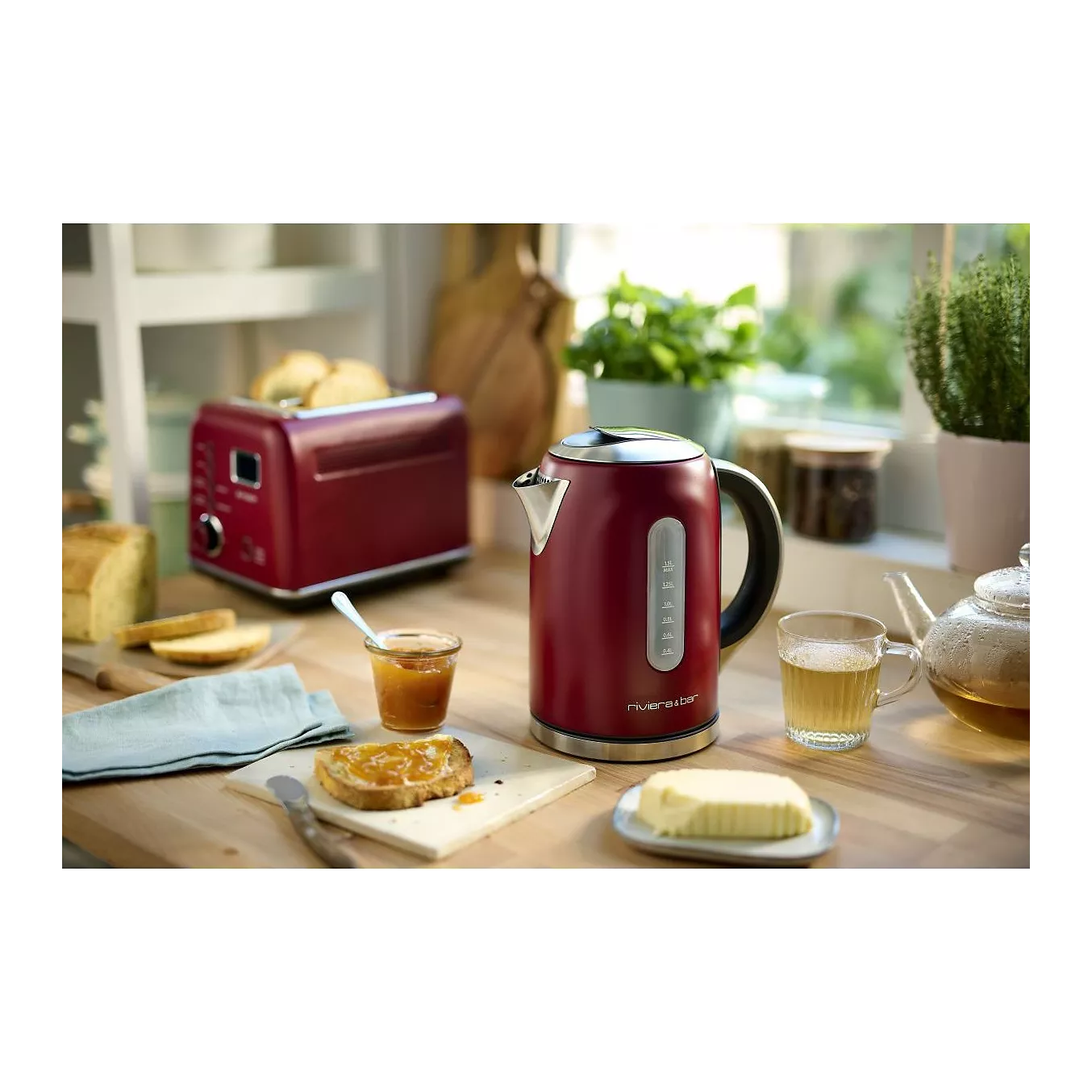 La bouilloire et le grille-pain rouges RIVIERA & BAR BBT577 sont posés sur un comptoir de cuisine en bois, entourés de thé, de miel, de pain et de beurre.