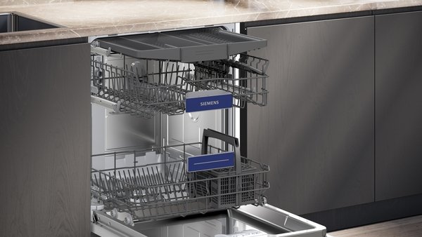 Un lave-vaisselle SIEMENS SN63E800VE avec des grilles étendues se trouve ouvert sous un comptoir en marbre dans une cuisine moderne.