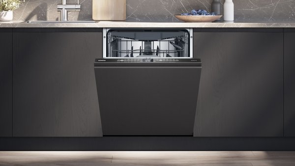 Un lave-vaisselle encastrable SIEMENS SN63E800VE avec la porte ouverte, installé dans une cuisine moderne avec des armoires sombres et un comptoir en marbre.