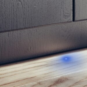Une petite lumière bleue brille sur un sol en bois près d'un meuble sombre, indiquant subtilement l'efficacité silencieuse du lave-vaisselle encastré SIEMENS SN63E800VE qui s'y trouve.