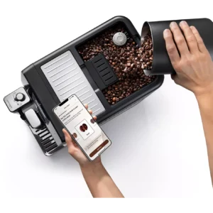 Une personne verse des grains de café dans la machine à café DELONGHI ELETTA EXPLORE ECAM470.85.MB et la contrôle à l'aide d'une application pour smartphone.