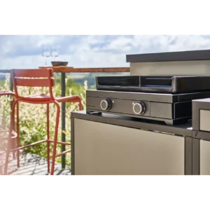 Gril en plein air sur un patio avec une plancha FORGE ADOUR MODERN E60 AN, avec un tabouret de bar rouge et des verres à vin sur une table en arrière-plan.