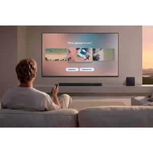 Une personne est assise sur un canapé et utilise une télécommande pour interagir avec le téléviseur mural SAMSUNG TMR65R85H, qui affiche un écran de sélection.