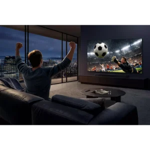 Une personne applaudit sur un canapé tout en regardant un match de football sur le téléviseur SAMSUNG TMR65R95H dans un salon moderne, la nuit.