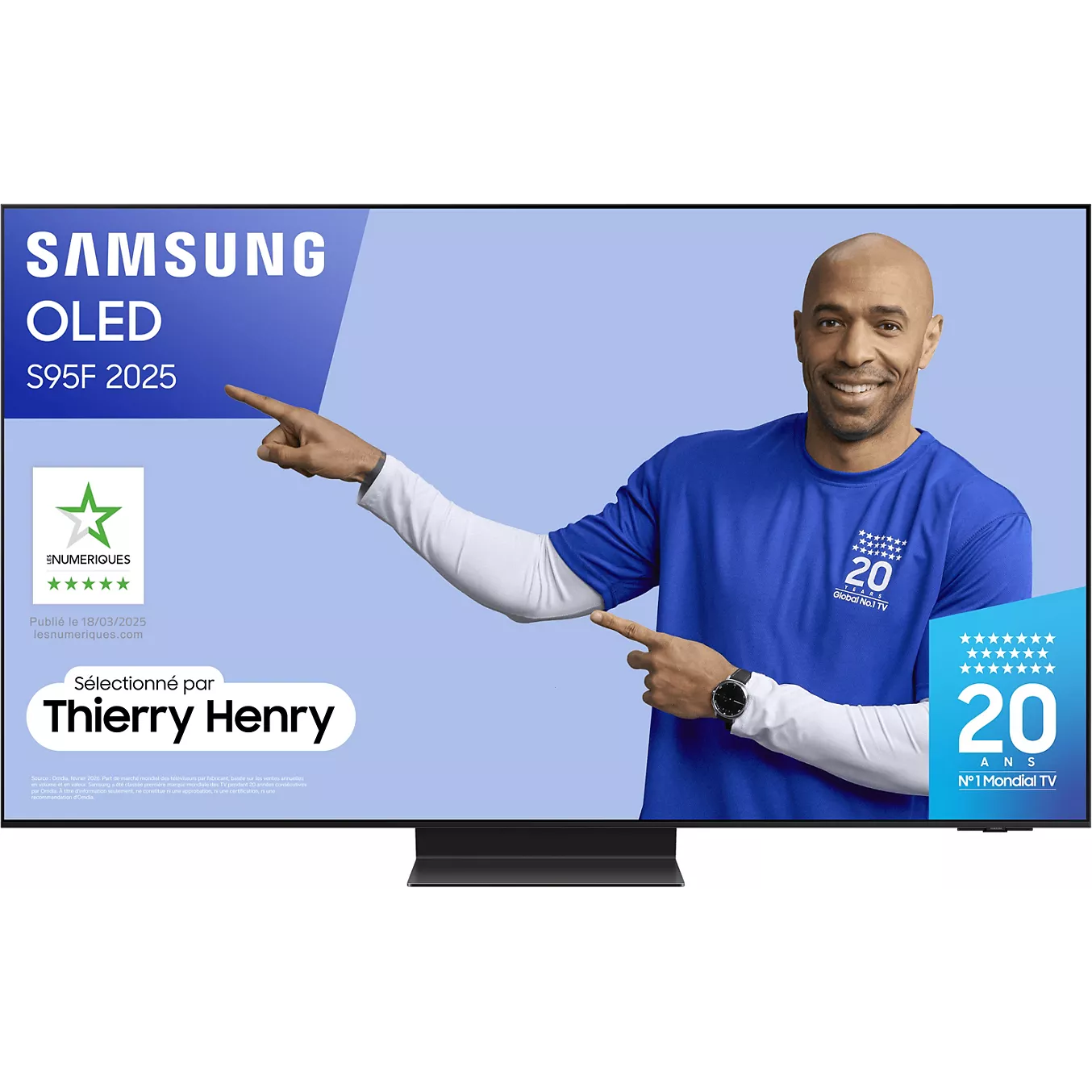 Un homme en chemise bleue montre un téléviseur Samsung affichant le modèle SAMSUNG TQ55S95F, avec des logos visibles et le texte "Thierry Henry" sur l'écran.