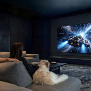 Un couple et leur chien regardent un film sur les vaisseaux spatiaux sur le SAMSUNG TQ65S95H dans un salon moderne et sombre.