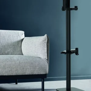 Dans une pièce moderne aux murs et à la moquette bleus, un canapé gris minimaliste côtoie une ROWENTA DOCKING STATION 7 aux lignes épurées et un grand support de sol noir.