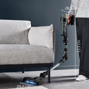 Une personne nettoie le dessous d'un canapé avec le manche flexible de l'aspirateur sans fil ROWENTA RH7A32E0, tandis que des étiquettes de dimensions mettent en évidence la zone pour référence.