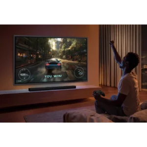 Une personne fait la fête sur son canapé après avoir gagné un jeu vidéo de course automobile sur un grand écran de télévision SAMSUNG TQ65S95H (Copie).