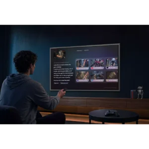 Une personne utilise une télécommande pour interagir avec un téléviseur mural SAMSUNG TQ65S95H (Copie) affichant un contenu de jeu dans une pièce sombre.