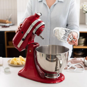 Dans la cuisine, quelqu'un utilise le robot pâtissier KITCHENAID 5KSM175PSEFL et tient son fouet rempli de crème fraîchement fouettée.