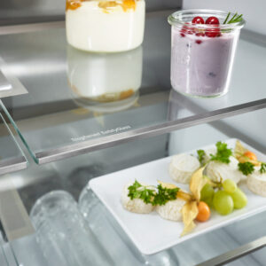 Une étagère du LIEBHERR MBSDDI9524-20 accueille des pots de yaourt ainsi qu'une assiette garnie de fromage, de raisins et d'accompagnement.
