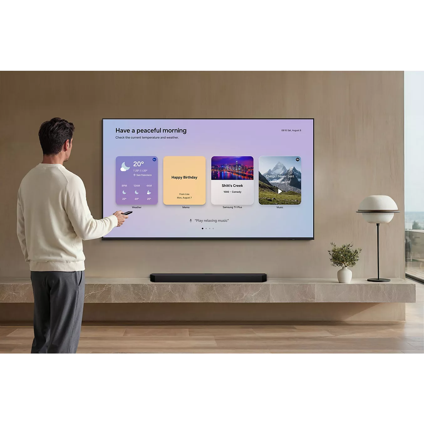 Un homme se tient devant un grand téléviseur SAMSUNG TMR75R85H fixé au mur, dont l'écran aux couleurs vives affiche les prévisions météo et des rappels.