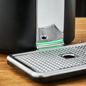 Gros plan sur un bac d'égouttage métallique aux lignes épurées posé sur une surface en bois, à côté de la machine à café KRUPS YY4808FD.