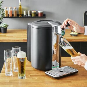 Quelqu'un verse de la bière à partir d'une tireuse KRUPS YY4808FD dans un verre posé sur un plan de travail en bois, à côté de deux verres déjà remplis.