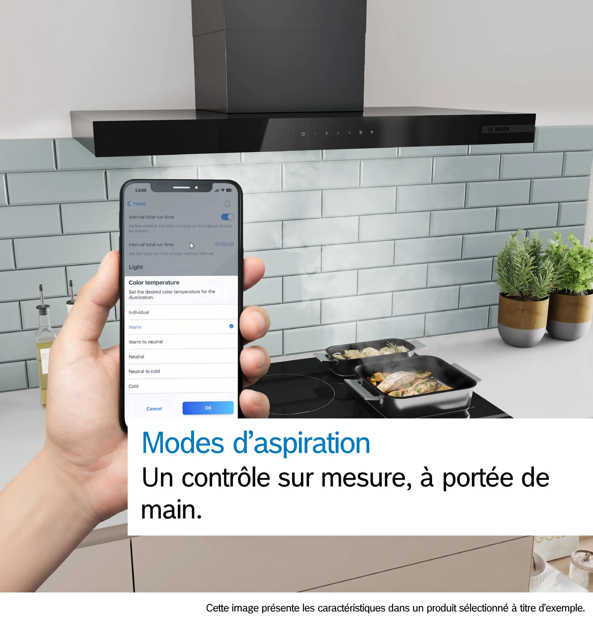 Une main tient un téléphone qui commande la hotte de cuisine DWB97DN, située au-dessus d'une cuisinière sur laquelle se trouvent une casserole et une poêle. Un texte en français s'affiche à l'écran.