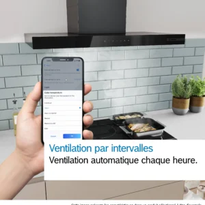 Une main tenant un téléphone sur lequel est ouverte une application de domotique, tandis qu'une personne cuisine du poisson sur la cuisinière, sous la hotte moderne DWB97DN installée dans la cuisine.