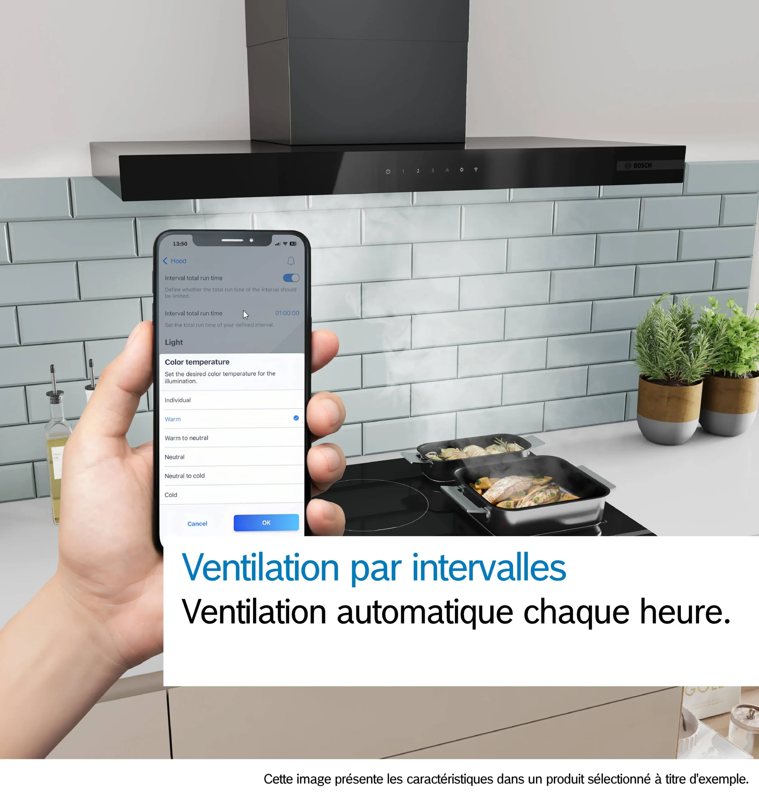Une main tenant un téléphone sur lequel est ouverte une application de domotique, tandis qu'une personne cuisine du poisson sur la cuisinière, sous la hotte moderne DWB97DN installée dans la cuisine.