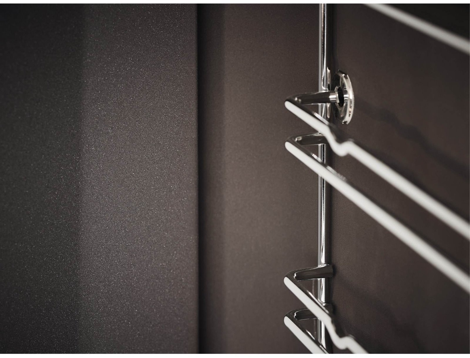Gros plan sur un porte-serviettes métallique brillant fixé à un mur sombre et lisse, qui rappelle les éléments de design épurés du four ELECTROLUX EOF3C40TH.