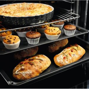 Trois grilles de four, sur lesquelles sont disposés une tarte, des muffins et des miches de pain, sont en train de cuire dans le four moderne ELECTROLUX EOF3C40TH.