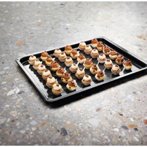 Une plaque de cuisson sur laquelle sont disposées des rangées de mini-cupcakes assortis, tout juste sortis du four ELECTROLUX EOF3C40TH, repose sur un plan de travail moucheté.