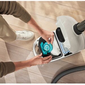 Personne en train de remplacer un sac d'aspirateur Miele GUARD S1 BLEU NORDIQUE FLEX sur un parquet clair, vue d'en haut.
