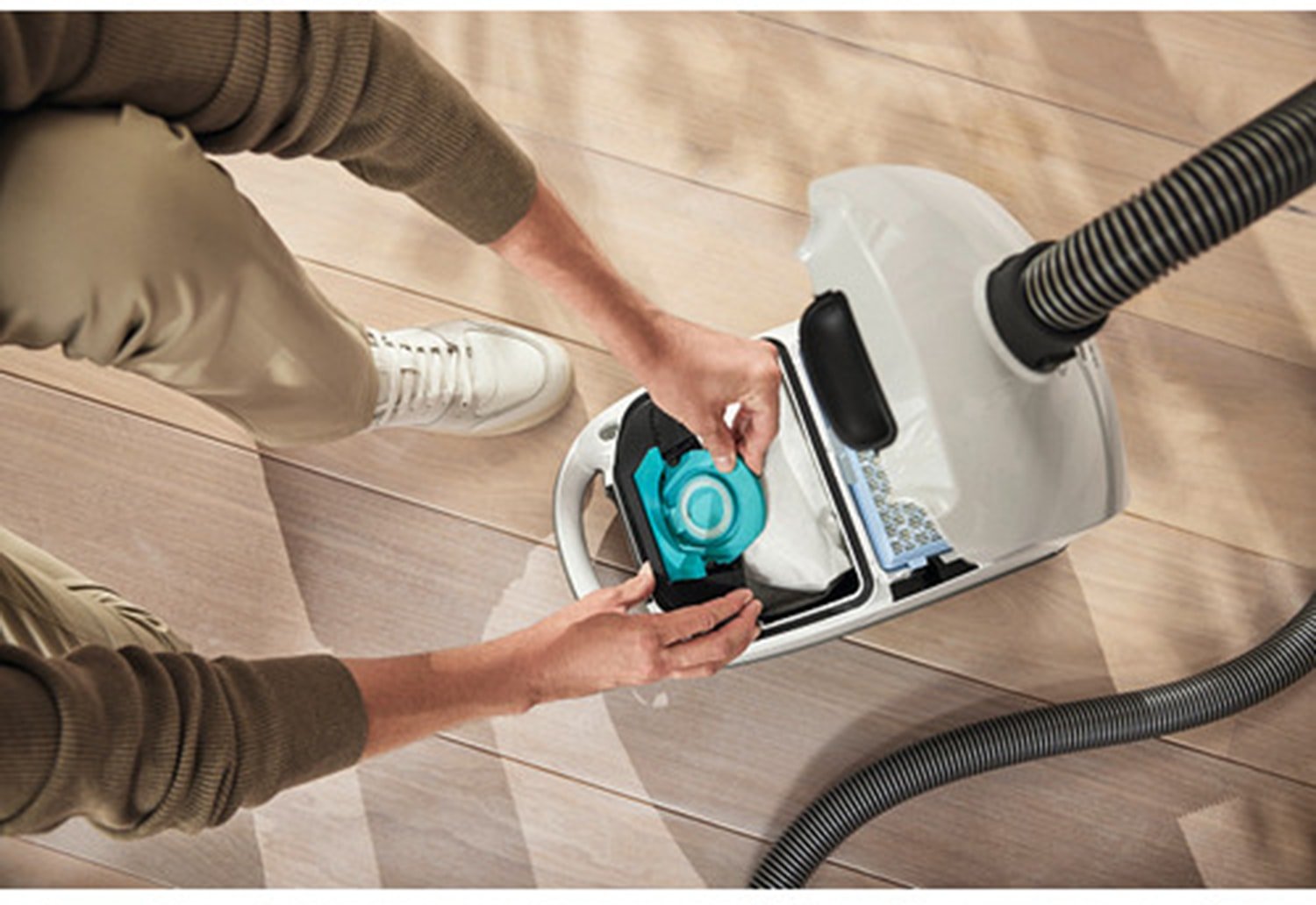 Personne en train de remplacer un sac d'aspirateur Miele GUARD S1 BLEU NORDIQUE FLEX sur un parquet clair, vue d'en haut.