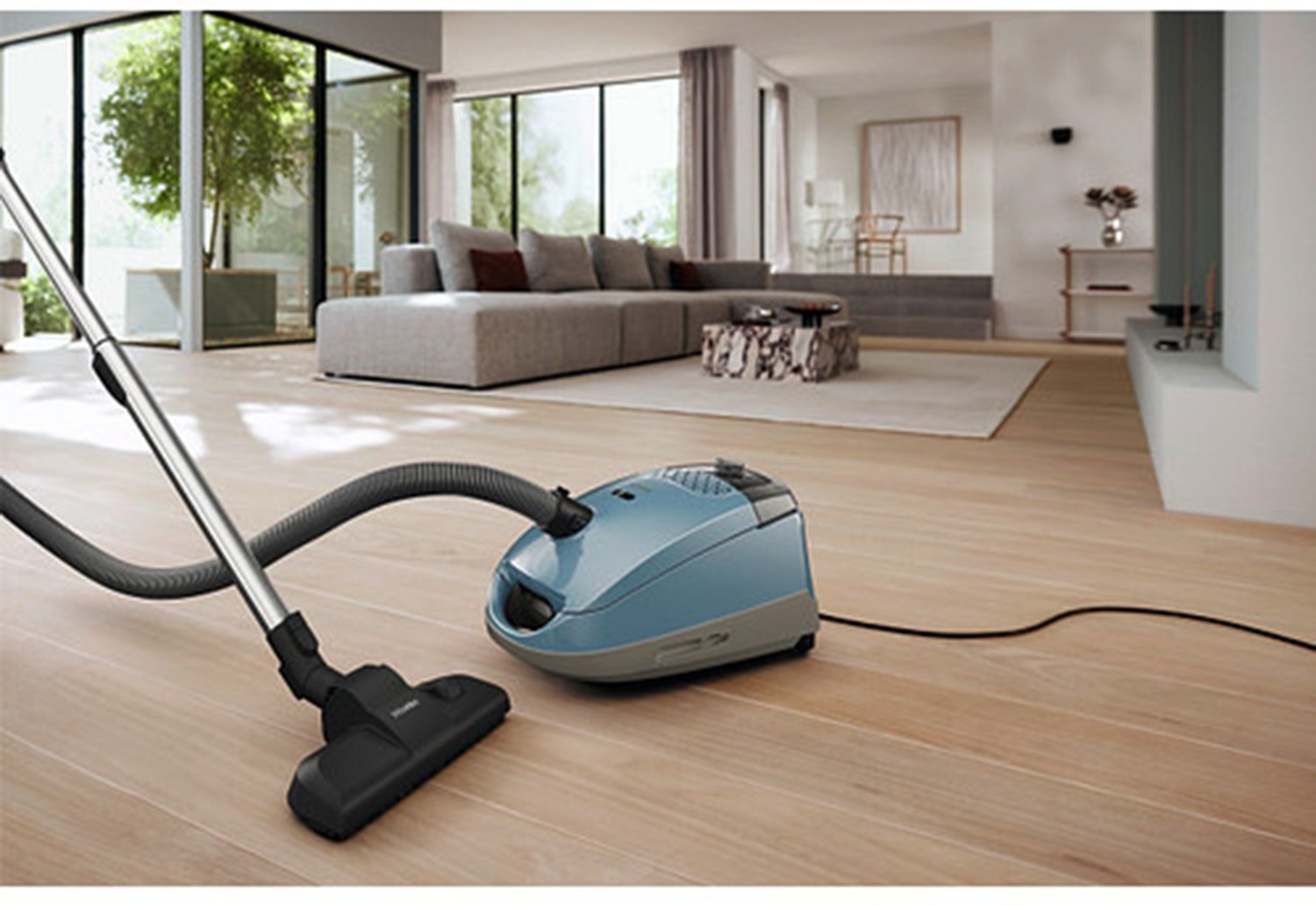 Un aspirateur-traîneau Miele GUARD S1 BLEU NORDIQUE FLEX est posé sur un parquet dans un salon moderne et lumineux.