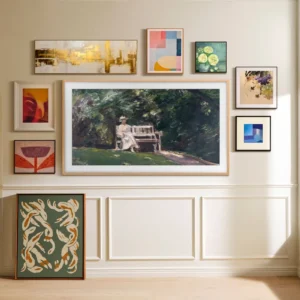 Un mur-galerie présentant une sélection d'œuvres d'art encadrées, notamment des peintures et des œuvres abstraites, est agencé avec goût au-dessus d'une lambris blanc et intègre harmonieusement le téléviseur SAMSUNG TQ65LS03HW dans l'ensemble.