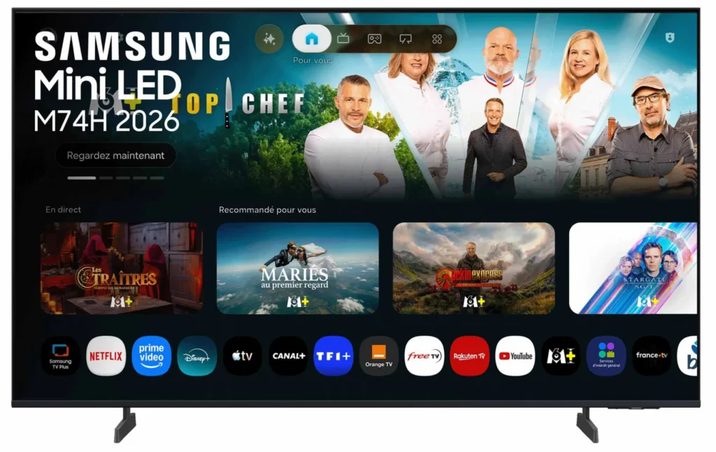 Un téléviseur SAMSUNG TU50M74H affiche un menu de streaming proposant des applications, avec en arrière-plan une émission culinaire mettant en scène quatre chefs et un animateur.